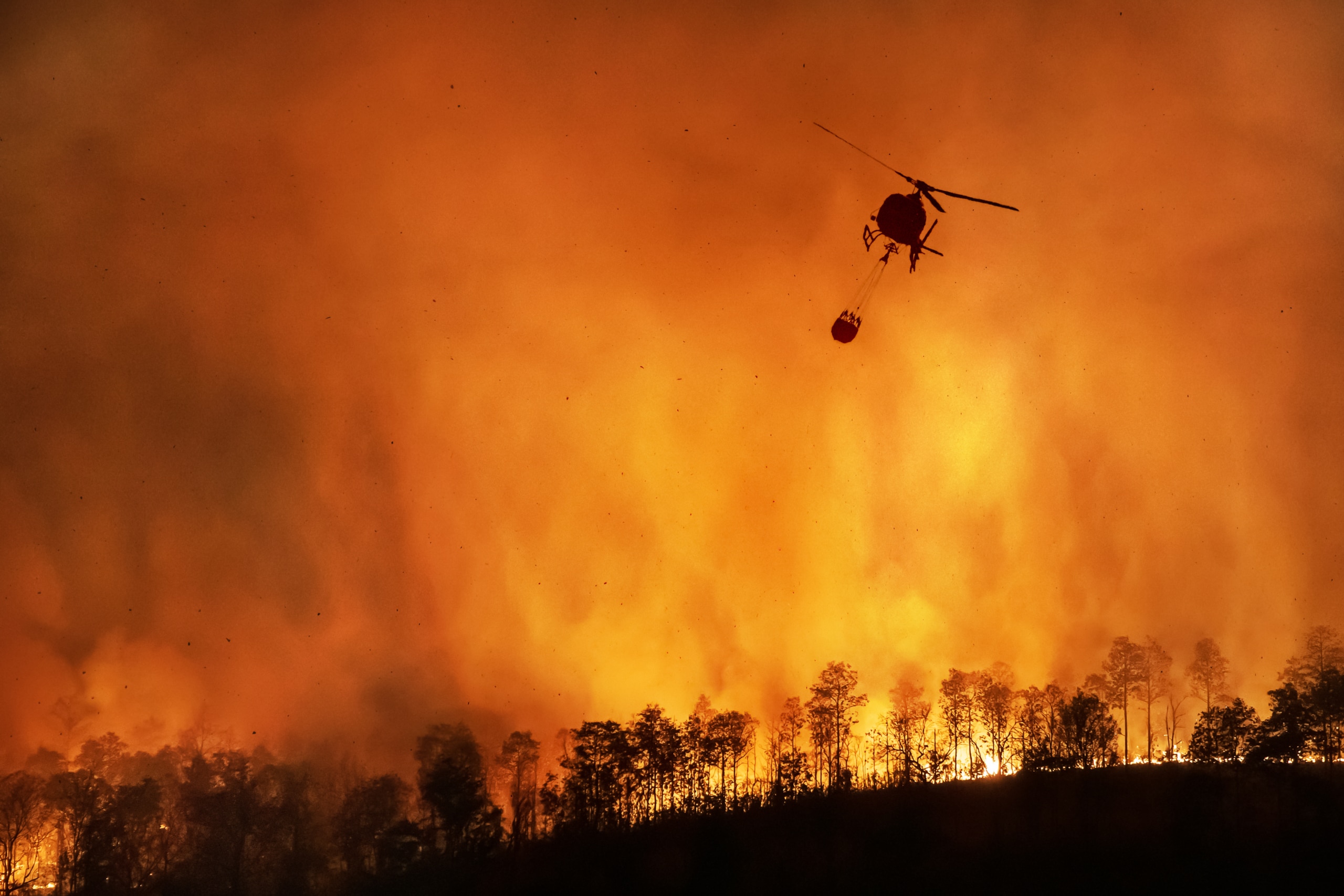 a helicopter deploying water over a forrest fire