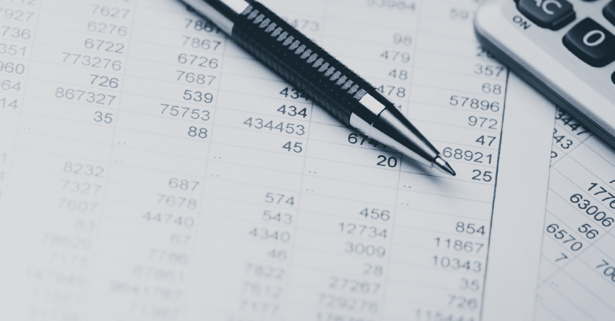 Two white pieces of paper, with spreadsheets printed on them with black ink, are laying on top of each other. There is a silver mechanical pencil with a black grip on top of one paper and a four function calculator on top of the other