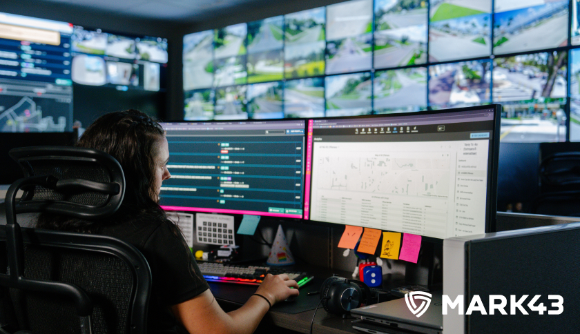 A Mark43 team member working on multiple computers and the Mark43 logo at the bottom corner