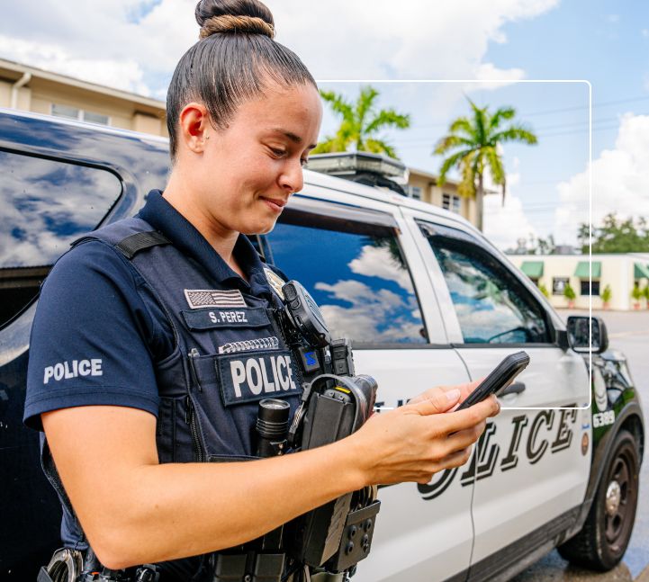 Police officer standing by their car using a smart phone